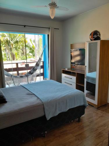 a bedroom with a bed and a tv and a window at Pousada Carambu in São Francisco do Sul