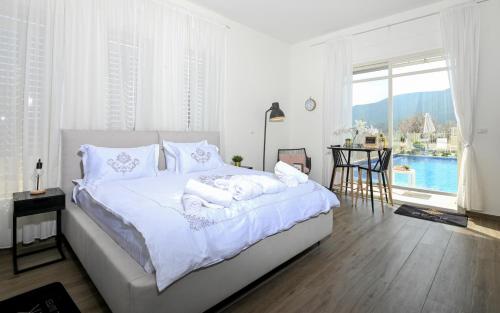a white bedroom with a large bed and a large window at סוויטות Peak - סוויטות מדהימות עם בריכה במתחם in Sifsufa