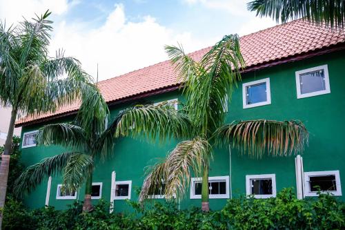 a green building with palm trees in front of it at Flats 2 Locação Penedo RJ in Penedo