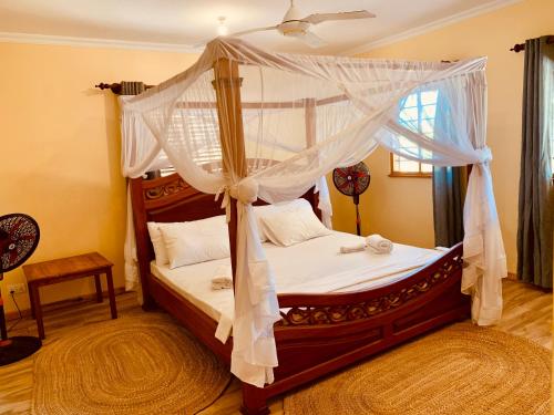a bedroom with a canopy bed with white curtains at Ushongo Beach Cottages - Family House in Tanga