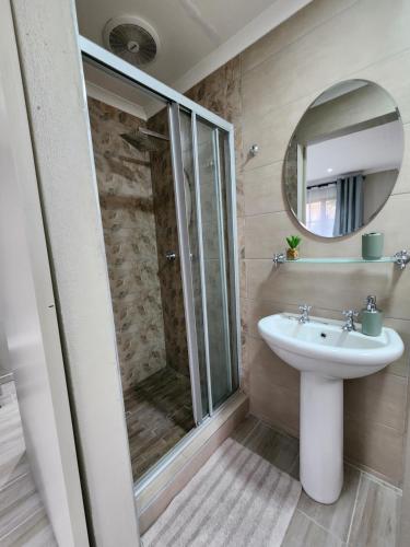 ein Bad mit einer Dusche, einem Waschbecken und einem Spiegel in der Unterkunft Cozy and Comfort in Harrismith