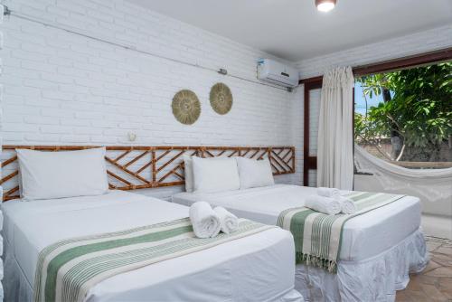 two white beds in a room with a window at Pousada Barra Sol in Barra de São Miguel