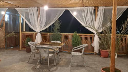 eine Terrasse mit einem Tisch, Stühlen und Vorhängen in der Unterkunft Naqshband in Buxoro