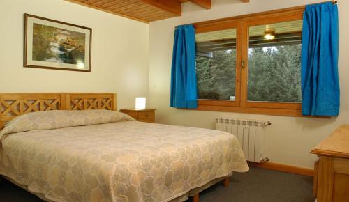een slaapkamer met een bed met blauwe gordijnen en een raam bij Cabañas Carelmapu in Bariloche