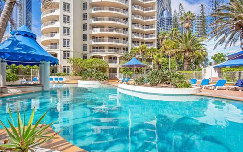 een zwembad met blauwe stoelen en een groot gebouw bij The Moroccan - QStay in Gold Coast