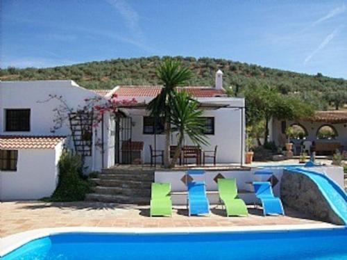 una casa con una piscina con sillas verdes y azules en Casa dos ponies, en Ríogordo