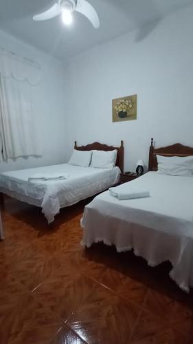 two beds in a room with white walls and wooden floors at Pousada Santo Expedito in Tiradentes