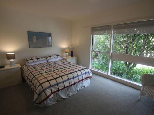 a bedroom with a bed and a large window at Hosts on the Coast - Vista Verde in Pauanui