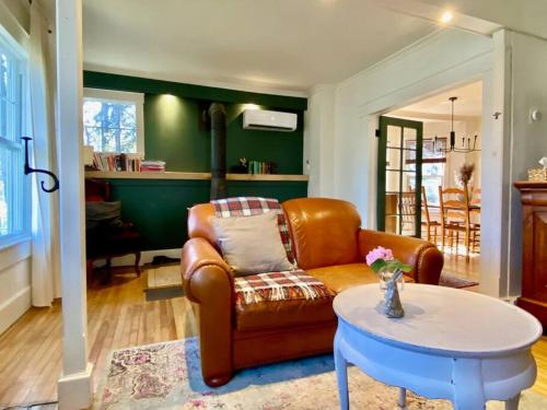sala de estar con sofá de cuero y mesa en Cozy Grey Rabbit House 20mn from Mount Orford Ski Resort, en Ayers Cliff