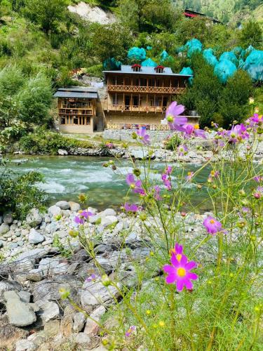 a building next to a river with flowers at Living Good - A Himalayan Boutique Stay in Gushaini