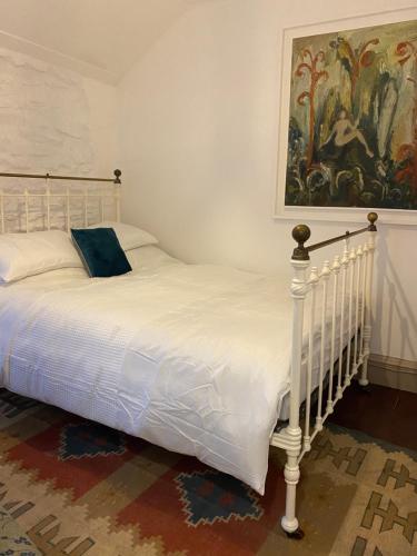 a bedroom with a white bed with a painting on the wall at The Painter’s Retreat in Lower Boscaswell