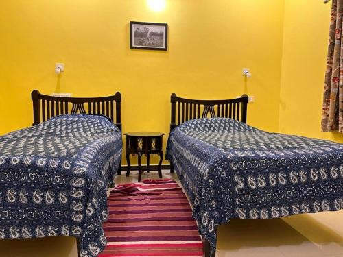 two beds in a room with a yellow wall at Sharad Baug homestay in Bhuj