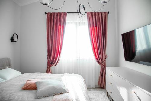 a bedroom with a bed and a window with red curtains at First Apartments in Focşani