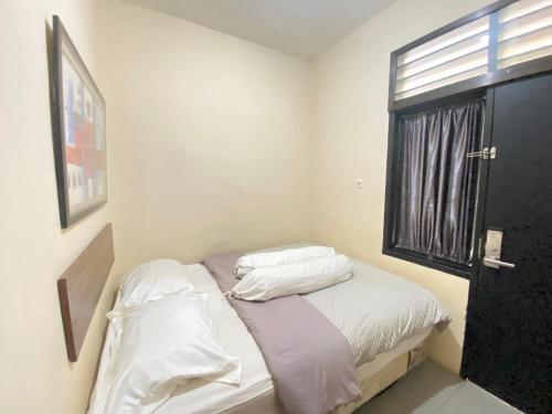 una camera da letto con un letto con lenzuola bianche e una finestra di De Homestay Mitra RedDoorz Bitung a Bitung