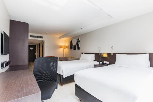 a hotel room with two beds and a chair at Maitria Hotel Sukhumvit 18 Bangkok – A Chatrium Collection in Bangkok