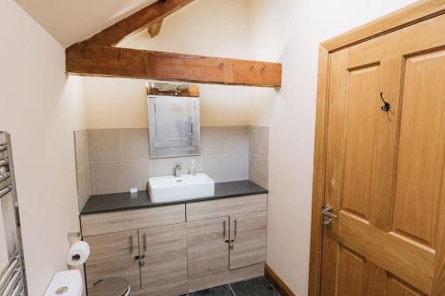 a bathroom with a sink and a wooden door at ELM HOUSE BARN - Converted One Bed Barn at the gateway to the Lake District National Park in High Hesket