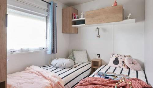 - 2 lits dans une petite chambre avec fenêtre dans l'établissement Camping la Haie Penée ****, à Saint-Quentin-en-Tourmont