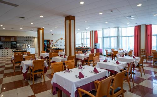 un restaurante con mesas y sillas blancas y ventanas en Medplaya Hotel Pino Alto, en Miami Platja