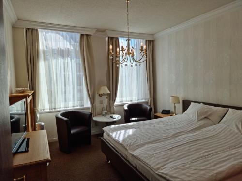 a hotel room with a bed and chairs and a chandelier at Hotel Beckröge in Cuxhaven