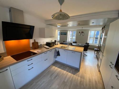 a kitchen with white cabinets and a flat screen tv at Appartement Les Corsaires in Granville