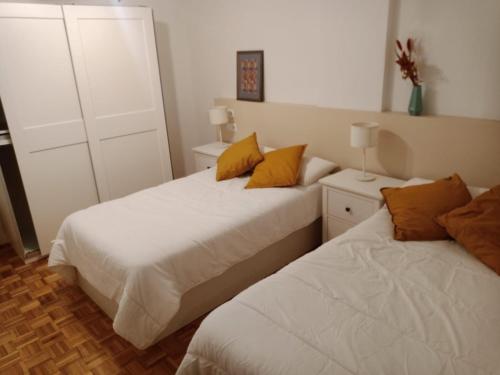 - 2 lits dans une chambre avec des oreillers blancs et jaunes dans l'établissement Piso playa Gijon, à Gijón