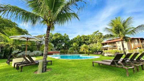 a pool with chairs and a palm tree and a house at Apartamento na Vila La Torre in Porto Seguro