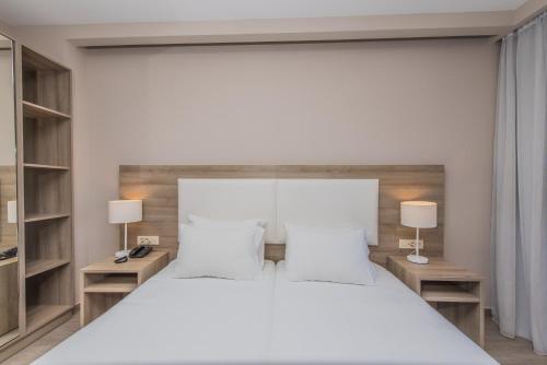 a bedroom with a large white bed and two lamps at Porto Planos Beach Hotel in Tsilivi