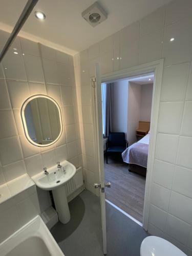 a bathroom with a sink and a mirror and a bed at The Westlynne Hotel & Apartments in Manchester