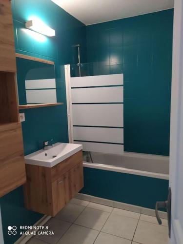 La salle de bains est pourvue de murs bleus, d'un lavabo et d'une baignoire. dans l'établissement Appartement bord de mer, à La Turballe