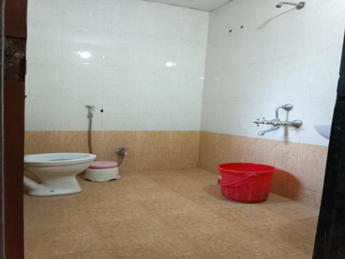 La salle de bains est pourvue de toilettes et d'un seau rouge. dans l'établissement Hotel Rachana Residency, à Pune