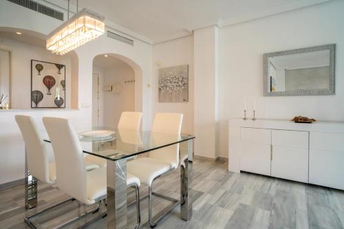 a dining room with a glass table and white chairs at El Lago de Los Arqueros 2 bedrooms penthouse en Benahavis in Benahavís