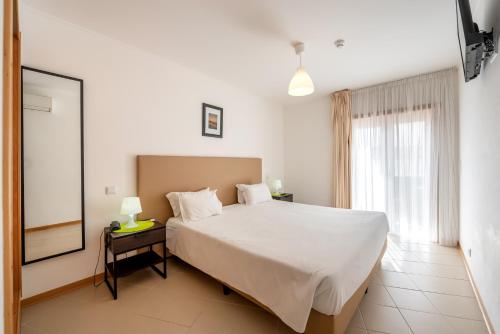 a bedroom with a large white bed and a window at Apartamentos Mirante da Rocha in Portimão