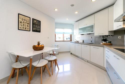 een keuken met witte kasten en een tafel en stoelen bij Spacious and Chic Apartment with Lisbon, Sintra, or Beach at 15 min! in Amadora