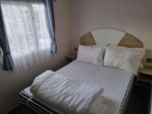 a bed with white sheets and pillows next to a window at 8 berth caravan PG214 Golden Palm Chapel st Leonards in Chapel Saint Leonards