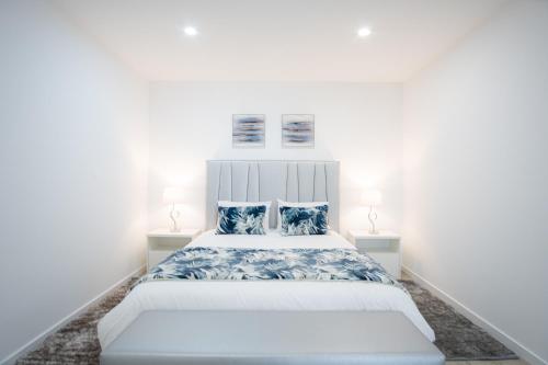 a white bedroom with a large bed with blue pillows at Casa Fonte Nova in Nazaré