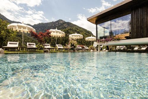 a large swimming pool with chairs and a building at Alpin Garden Luxury Maison & SPA - Adults Only in Ortisei