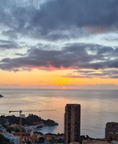 un coucher de soleil sur l'océan avec une ville et des bâtiments dans l'établissement Les terrasses de Beausoleil, à Beausoleil