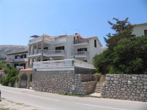a large white house with a stone wall next to a street at Apartments Tina in Pag