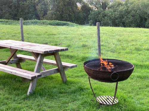 uma grelha ao lado de uma mesa de piquenique e um banco em Home Farm Radnage Glamping Bell Tent 6, with Log Burner and Fire Pit em High Wycombe