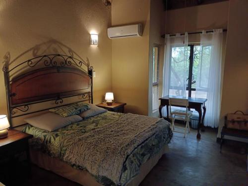 a bedroom with a bed and a desk and a window at Hoedspruit Bush Cottage in Hoedspruit