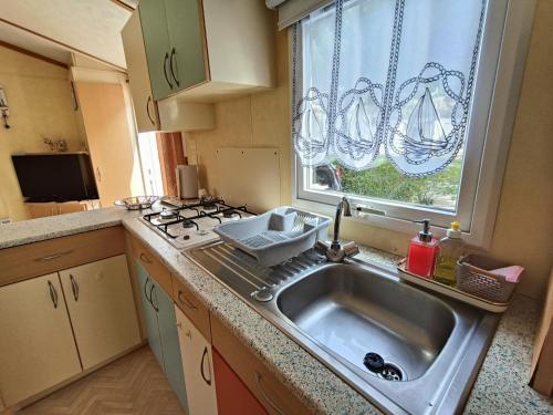une cuisine avec un évier, une cuisinière et une fenêtre dans l'établissement Mobilhome Oléron simple et spacieux à 1min de l'Océan, à La Cotinière