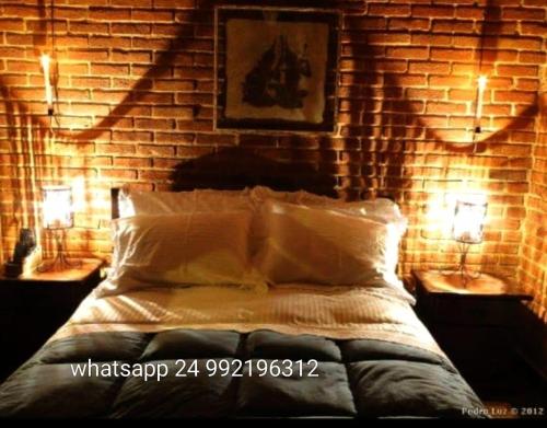 um quarto com uma parede de tijolos e uma cama com duas luzes em Pousada Romântica Serra da Mata em Penedo