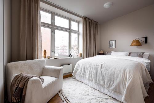 a bedroom with a white bed and a chair and a window at Hotel suite apartment in Oslo