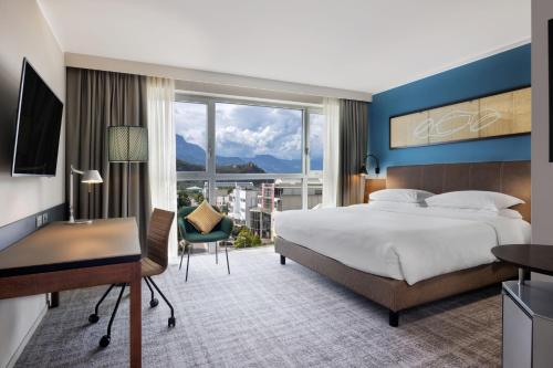 a bedroom with a bed and a desk and a large window at Four Points Sheraton Bolzano Bozen in Bolzano