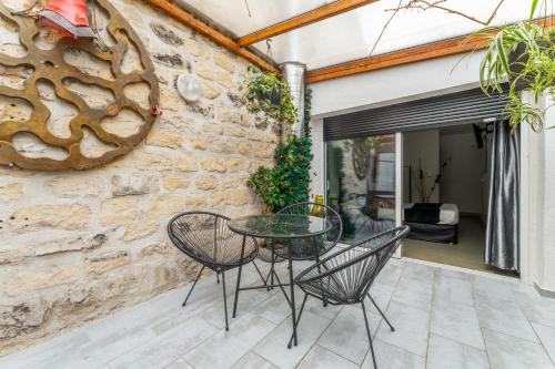 d'une terrasse avec une table et des chaises en verre devant un mur en pierre. dans l'établissement L'Oasis Montparnasse, à Paris