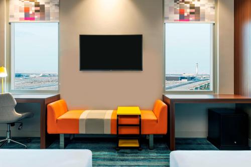 a waiting room with an orange chair and a flat screen tv at Aloft Dubai South in Dubai