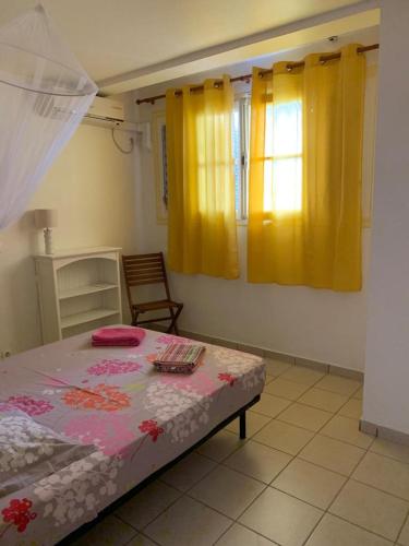 a bedroom with a bed and two windows with yellow curtains at LE JARDIN DE GABRIEL in Sainte-Anne