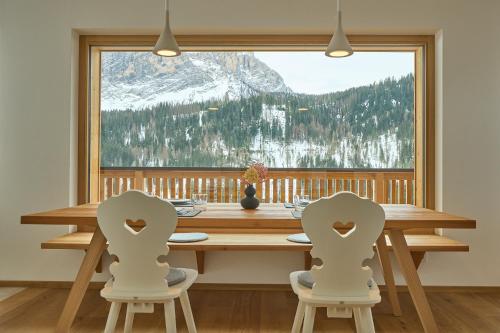 a dining room table with two chairs and a large window at Ciasa Plandros Apartments in La Valle