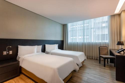 a hotel room with two beds and a desk at Tryp by Wyndham Belo Horizonte Savassi in Belo Horizonte