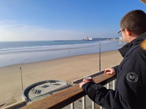 a man standing on a balcony looking at the beach at MIREILLE - Appartement 4 etoiles vue mer - 2 a 4 pers in Les Sables-dʼOlonne